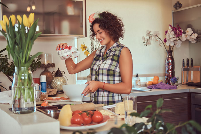 Woman cooking in a stylish kitchen with flowers, engaging in meal preparation, related to MIL and DIL dinner story.