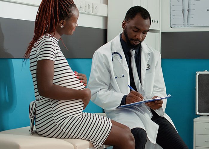 Pregnant woman at doctor's appointment, discussing notes with physician.