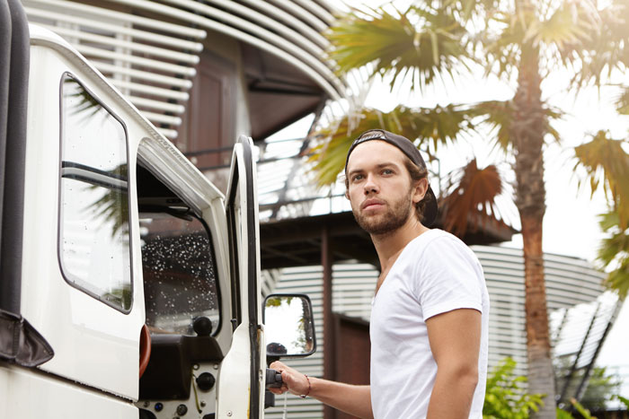 Man in white shirt standing by a truck, representing a job-hopper considering career options. Palm trees in the background.