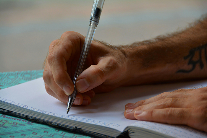 A man's hand writing in a journal, emphasizing sinister journal details. A man's hand writing in a journal, emphasizing sinister journal details.