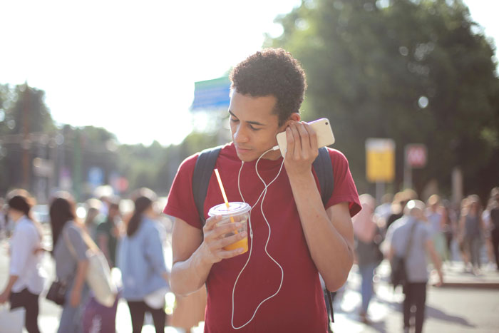 Young man with headphones holding a drink in a busy street, enjoying music.