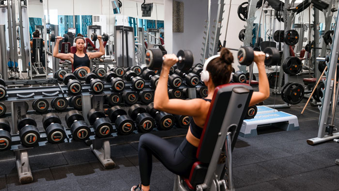 Woman wearing headphones lifting weights in the gym, using headgear while working out.