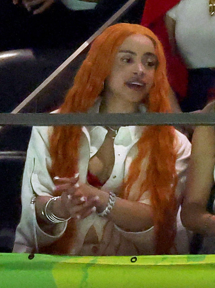 Woman in a white outfit with long orange hair, sitting at Super Bowl 2025, showcasing a head-turning look.