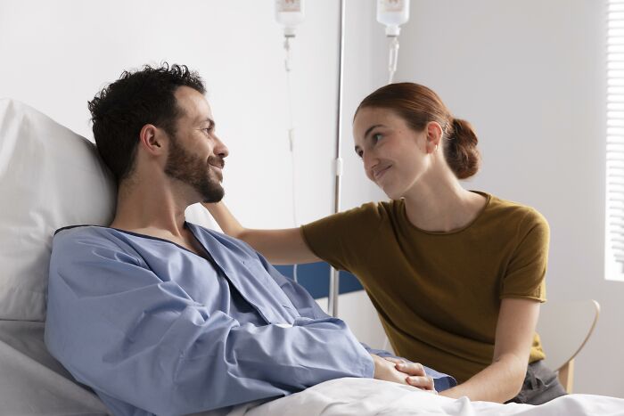 Woman lovingly supports man in hospital bed, showcasing deep love and care.