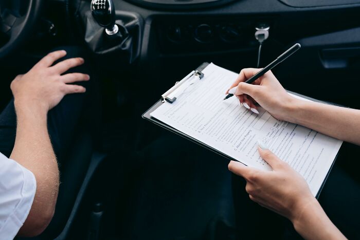 Person writing on a form inside a car, capturing a secretive moment.