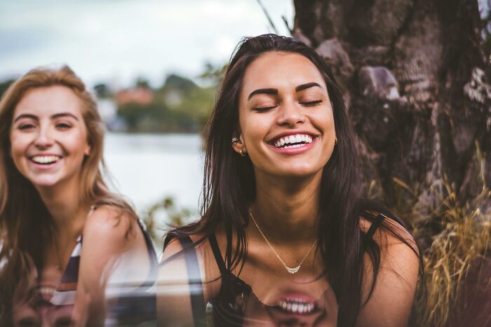Two women smiling outdoors, capturing a moment of joy, possibly pondering bizarre facts shared by netizens.