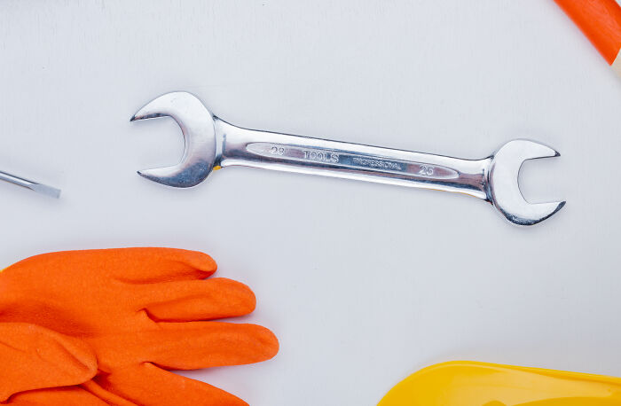 A shiny wrench on a white surface, with orange gloves and a yellow tray nearby, reflecting bizarre and forbidden secrets.