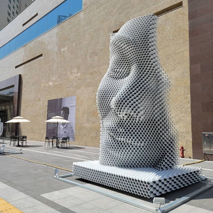 Metal pipe sculpture featuring a face by Yi Chul Hee, displayed outside a modern building.