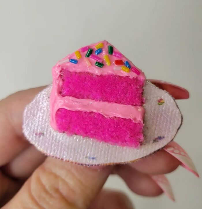 Hyper-realistic embroidered dessert resembling a slice of pink cake with colorful sprinkles, held in hand.