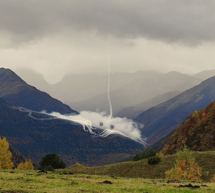 Whimsical cloud intervention by Vorja Sánchez in a misty mountain landscape, with artistic white accents and eyes.