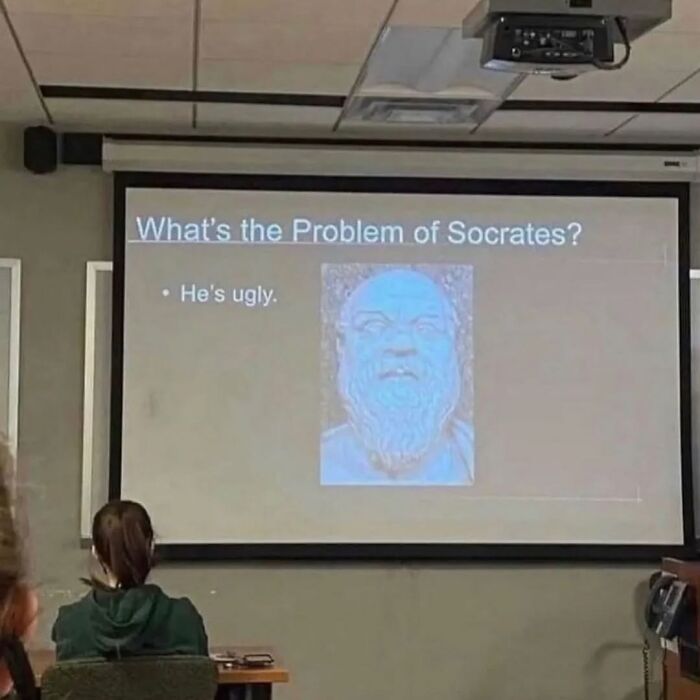 Proyección divertida en clase sobre el problema de Sócrates con texto humorístico en pantalla.