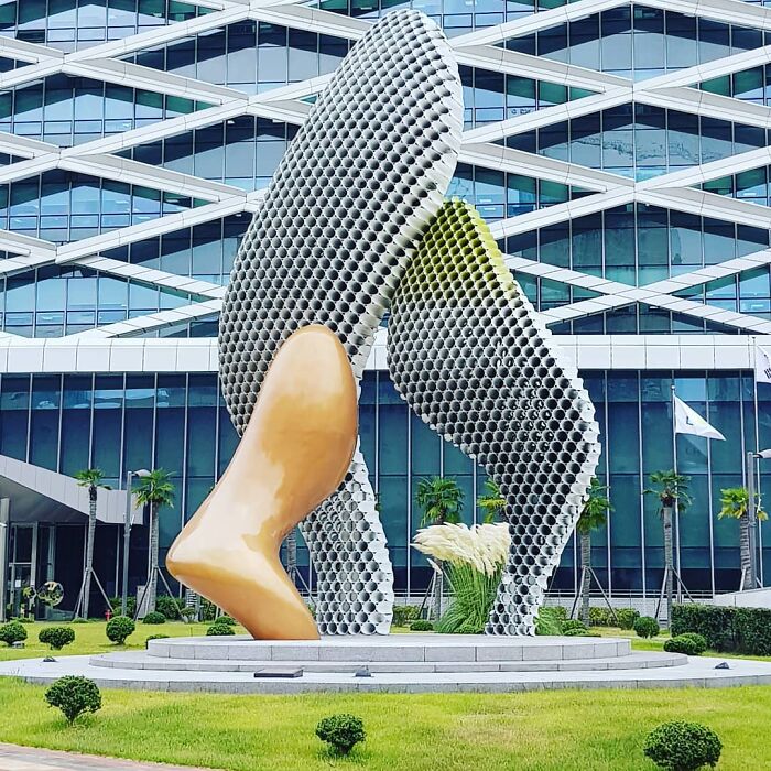 Metal pipe sculpture by Yi Chul Hee in front of a modern building with geometric patterns, surrounded by greenery.