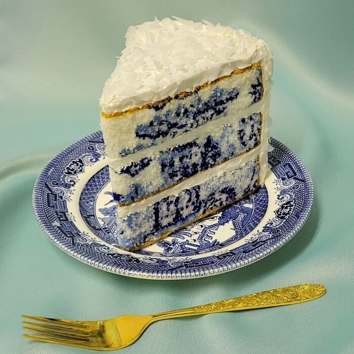 Hyper-realistic embroidered cake slice with blue patterns on a decorative plate, next to a gold fork.