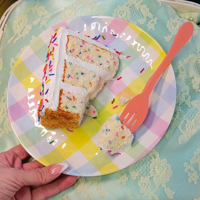 Hyper-realistic embroidered dessert resembling a cake slice on a pastel checkered plate with a pink fork.
