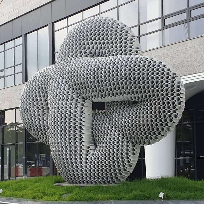 A captivating metal pipe sculpture by Yi Chul Hee, displayed outdoors in front of a modern building.