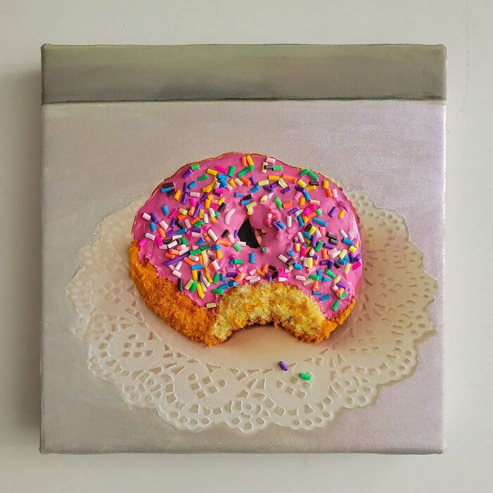 A hyper-realistic embroidered dessert depicting a donut with pink icing and sprinkles on a canvas.