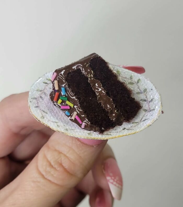 Hyper-realistic embroidered dessert resembling a chocolate cake slice with colorful sprinkles held in hand.