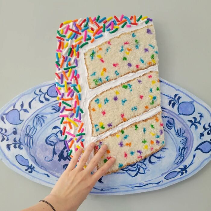Hyper-realistic embroidered dessert resembling a cake slice with colorful sprinkles, with a hand for scale.