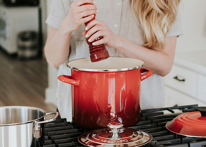 Person seasoning food in red cooking pot, demonstrating essential life skills in a modern kitchen setting