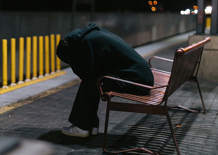 Person wearing a dark hoodie sitting alone on a bench at night, reflecting on must-have life skills and challenges.