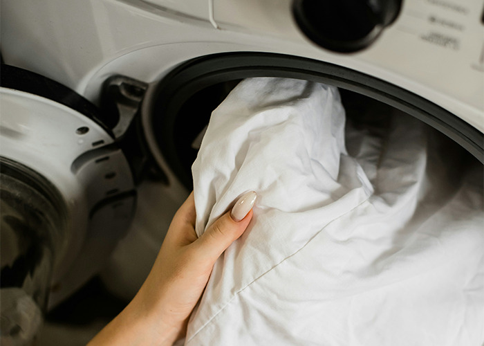 Person loading white laundry into a front-loading washing machine demonstrating must-have life skills.