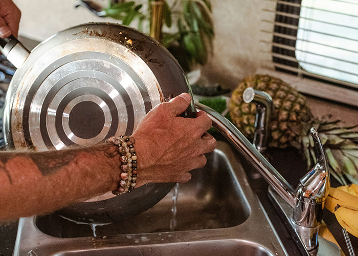 Person washing a pan in the kitchen sink, demonstrating essential life skills many internet users rarely learn.