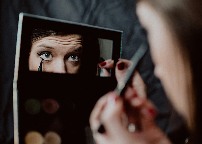 Woman applying eyeliner while looking into a mirror, demonstrating one of the must-have life skills for personal care.