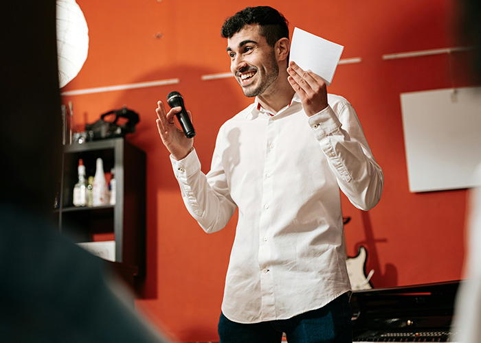 Young man demonstrating must-have life skills, holding a microphone and notes while speaking confidently indoors.
