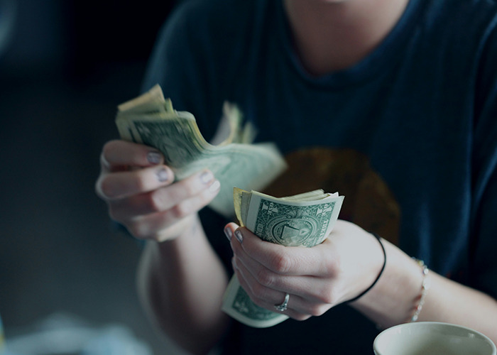Person counting US dollar bills wearing a dark shirt, illustrating essential money management life skills for internet users.