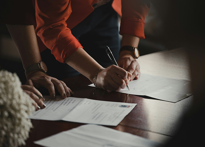 Person in red sleeves learning essential life skills like document signing at a wooden table.