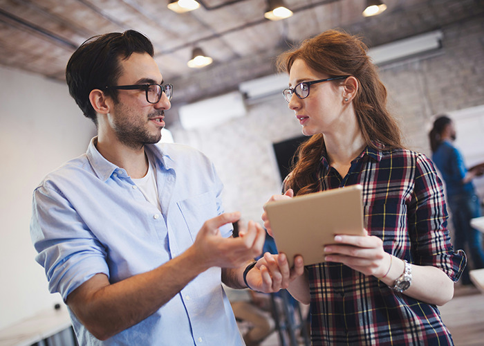Two people in discussion, practicing life skills, with one holding a tablet in a modern office setting.