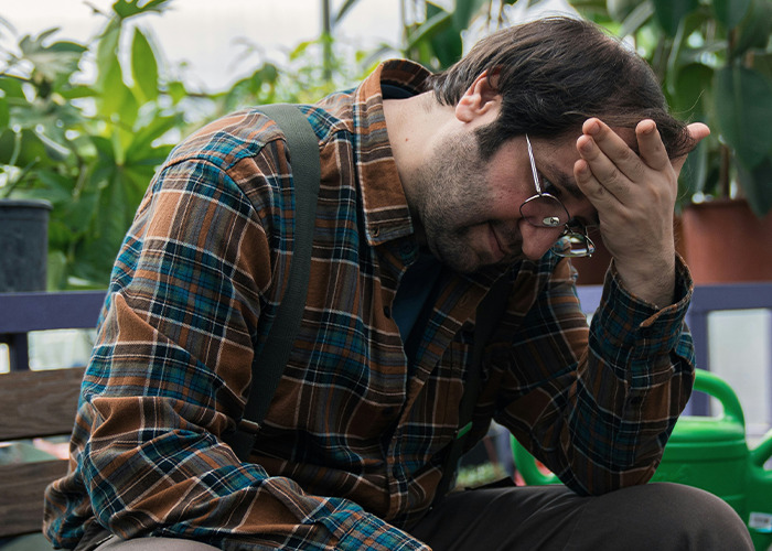 Man in glasses and plaid shirt sitting with hand on forehead, reflecting on must-have life skills and challenges.