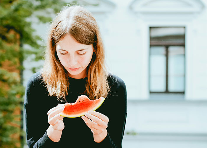 Young woman in a black sweater eating a slice of watermelon outdoors, illustrating must-have life skills concept.