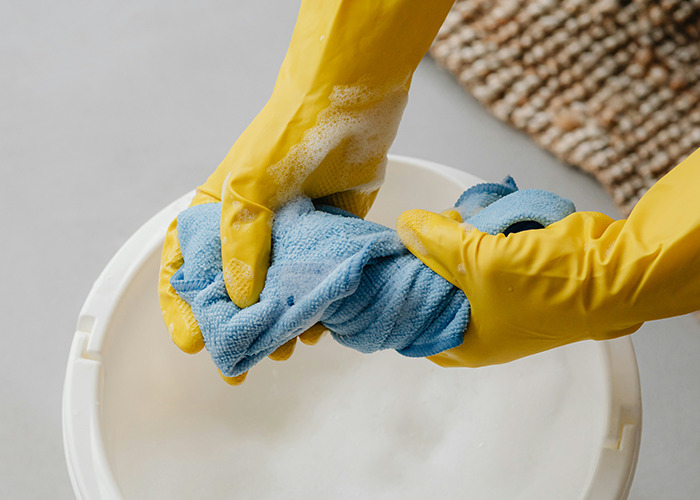 Person wearing yellow gloves wringing a wet blue cloth over a bucket, demonstrating essential life skills for internet users.