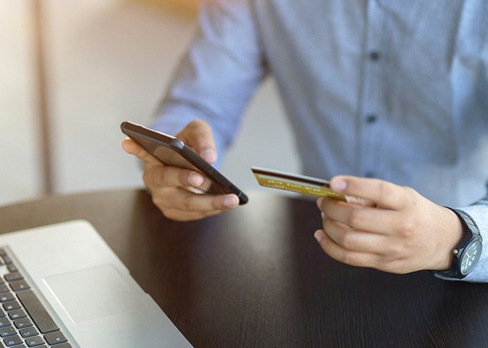 Person using smartphone and holding a credit card, illustrating essential life skills in modern technology usage.