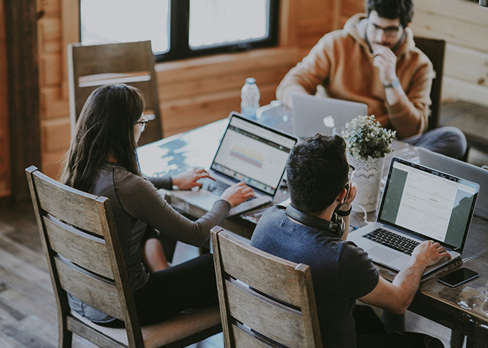 Three young adults using laptops in a wooden room, focusing on developing must-have life skills for internet users.