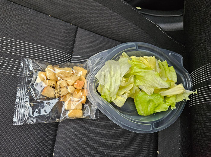 Lettuce in a bowl with packaged croutons on a seat, representing food scams.