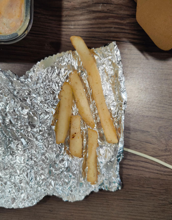 French fries served sparingly on foil, highlighting food scams with misleading portions.