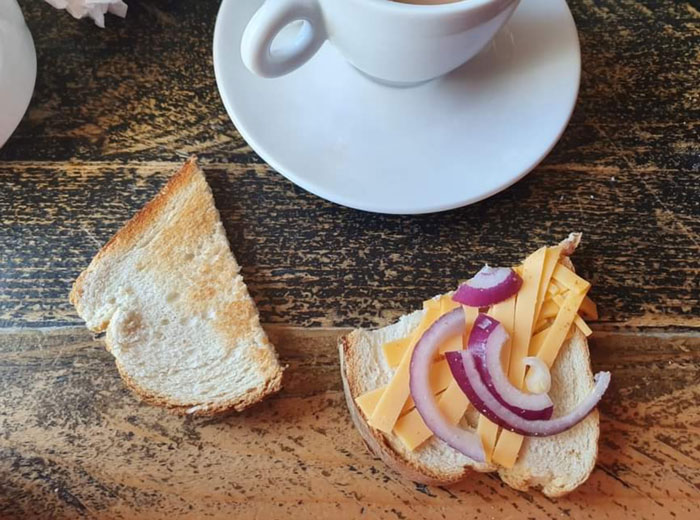 Open-faced sandwich with minimal cheese and onion next to coffee, illustrating food scams.