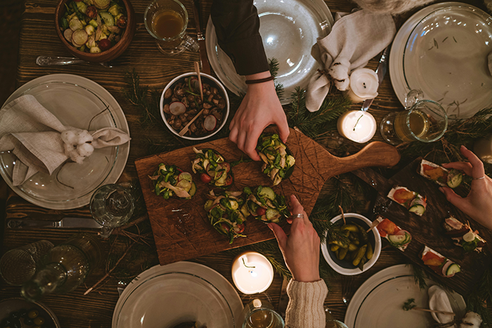 Family dinner scene with hands reaching for appetizers, highlighting a rustic meal setting with candles.