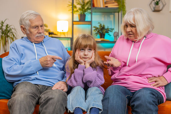 Elderly couple in colorful hoodies discussing with a pensive child on a sofa, illustrating harsh realities about life.