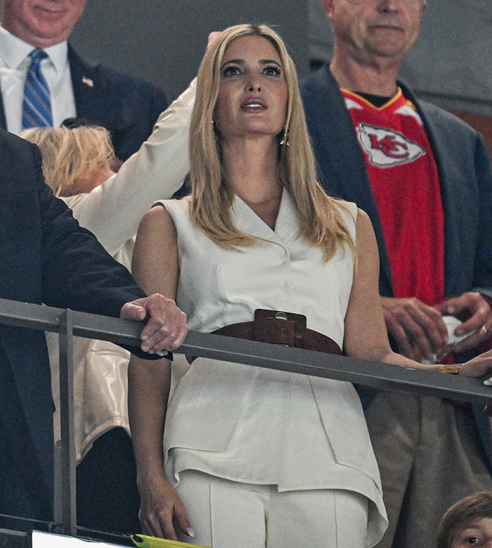 Ivanka Trump with long hair extensions at an event, wearing a white outfit, surrounded by people in a sports setting.