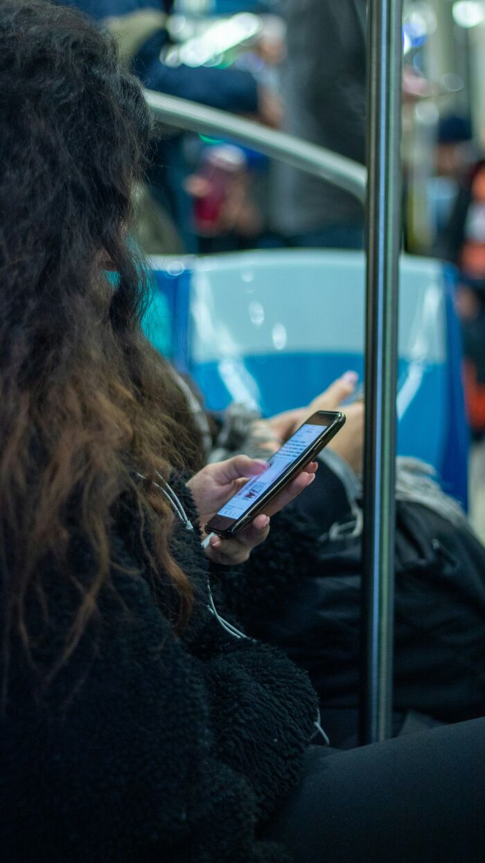 Gen Zer using a smartphone on public transport, engaging in conversation or browsing while commuting.