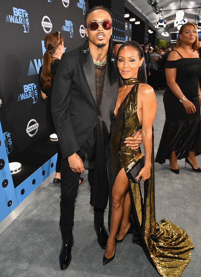 I don't know who these people are. A man in a black suit with sunglasses and a woman in a gold dress at an event.