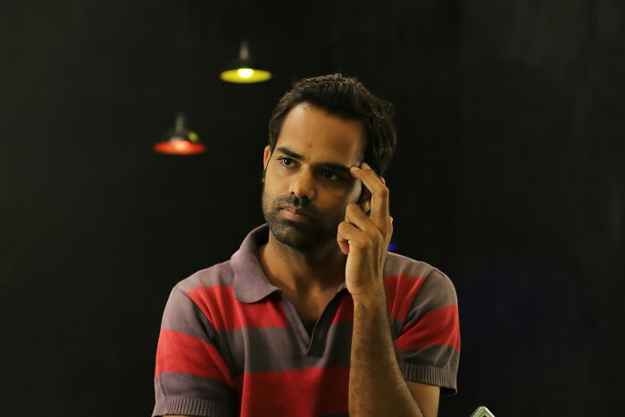 Man in a striped shirt pondering, symbolizing therapists' knowledge to change mindsets in a well-lit room.
