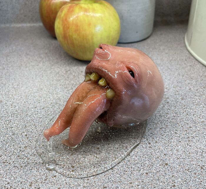 Creepy handmade craft resembling a distorted head on a countertop near apples.
