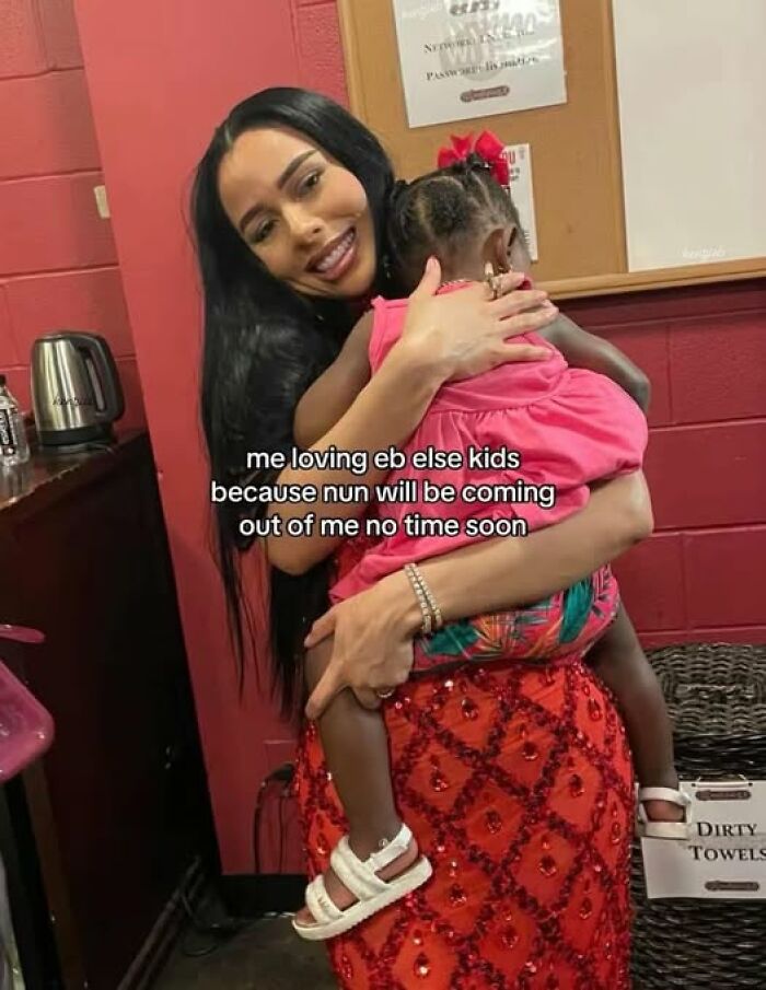 Woman in a red skirt holding a child, smiling, with humorous text about kids as a "Just Girly Things" meme.