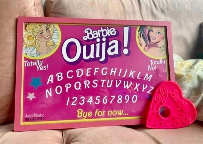 Barbie-themed Ouija board on pink couch, featuring alphabet and numbers, with a heart-shaped planchette.