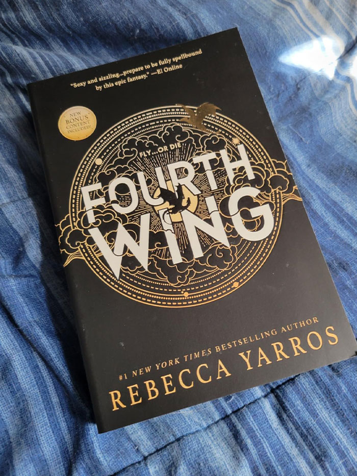 "Cover of the book 'Fourth Wing' by Rebecca Yarros on a blue fabric background, featuring book quotes."