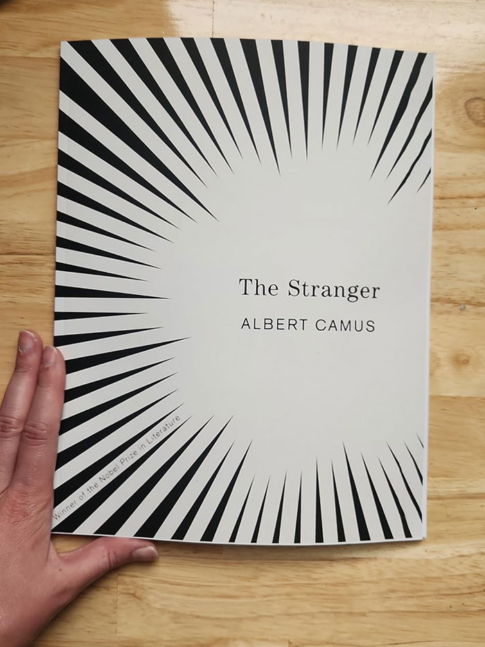 Cover of "The Stranger" by Albert Camus held on a wooden surface, related to book quotes.